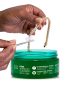 Hands cleaning a tennis bracelet with a jar of Fine Jewelry Cleaner