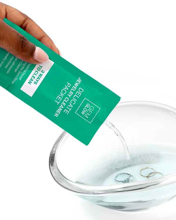 Hand pouring Jewelry Cleaner Packet into a glass bowl containing jewelry