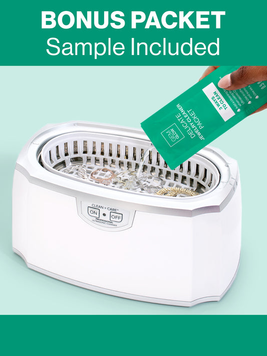 A hand pouring the bonus GEM GLOW cleaner packet sample into the Ultrasonic Jewelry Cleaner basin with jewelry submerged.